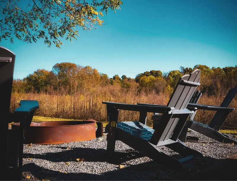 Adirondack chairs circled around the fire pit outside the Farm House Lodge, looking out over autumn treeline and bird fields